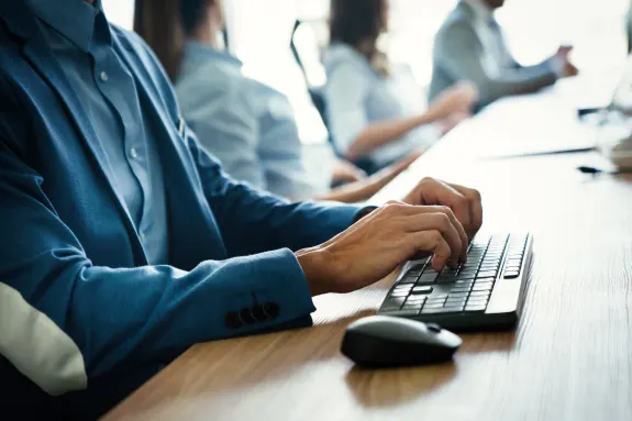 Office worker in blue suit typing on keyboard during a meeting.