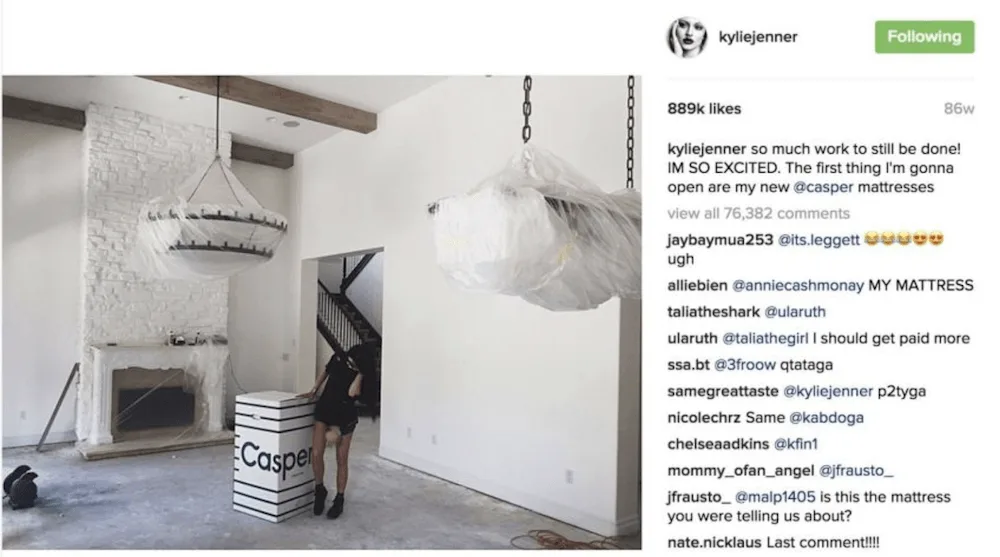 Woman standing next to a Casper mattress box in a living room with covered chandeliers.