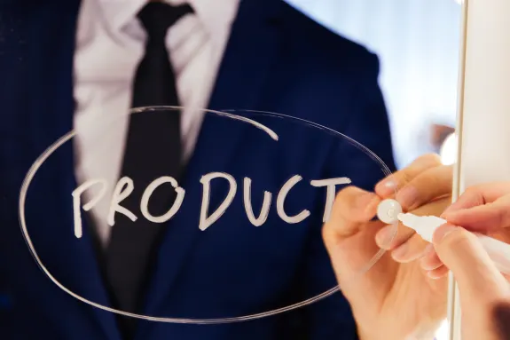 Person in a suit writing the word 'product' on a mirror with a white marker.