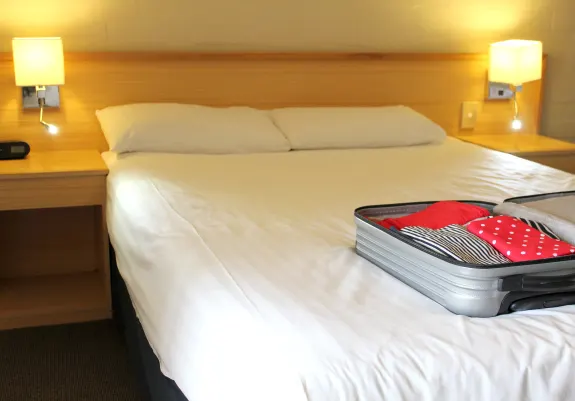 Hotel room with a neatly made bed, open suitcase, and lit lamp.