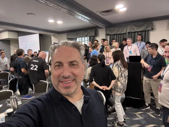Group of people networking at a conference with a presentation screen in the background.