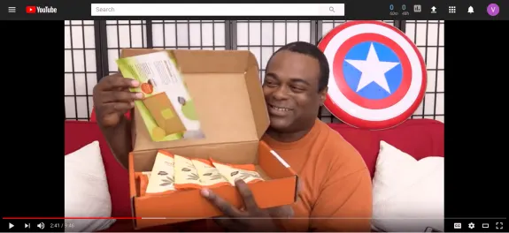 Man unboxing a snack box with a Captain America shield in the background.