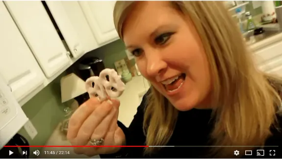 Woman holding yogurt-covered pretzels in a kitchen.