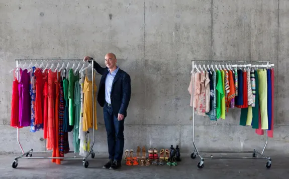 Man standing beside two racks of colorful clothes and shoes in a concrete room