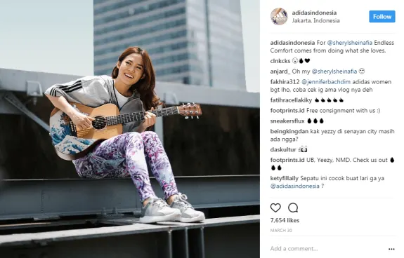 Woman smiling while playing guitar on a rooftop in a casual outfit.