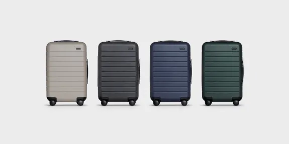 Set of four hard shell suitcases in beige, black, blue, and green on gray background.