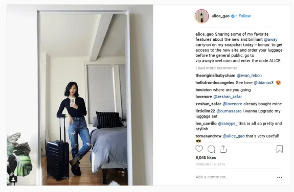 Woman taking a mirror selfie with a suitcase in a bedroom.