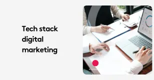 Two professionals at a desk with a laptop discussing digital marketing strategies.