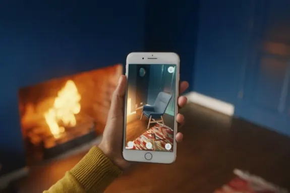 Hand holding smartphone using augmented reality app to view home decor in living room with fireplace.