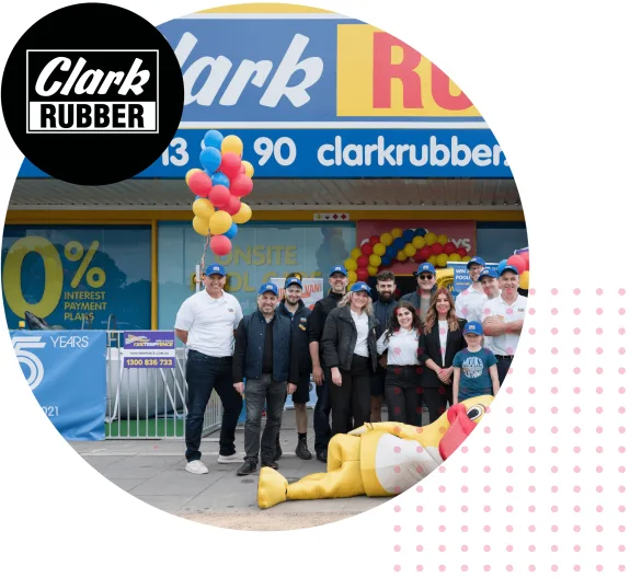 Group posing with balloons outside Clark Rubber store during an event.
