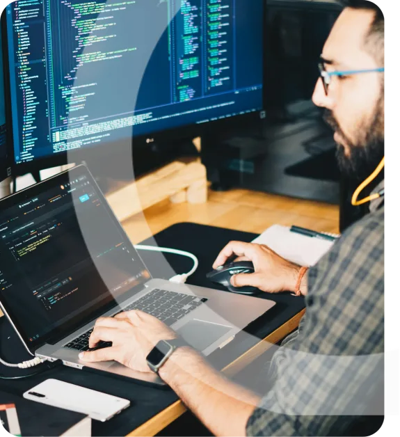 A software developer coding on a laptop with multiple screens displaying code.