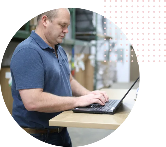 Man in blue shirt working on a laptop at a warehouse desk