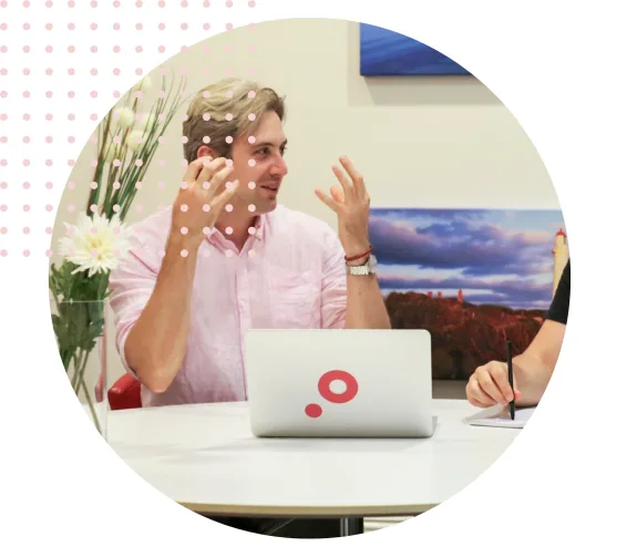 Man in pink shirt discussing work with a laptop during a meeting.