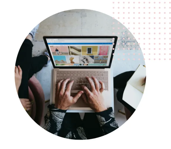 Person using a laptop to browse images during a meeting with others taking notes.