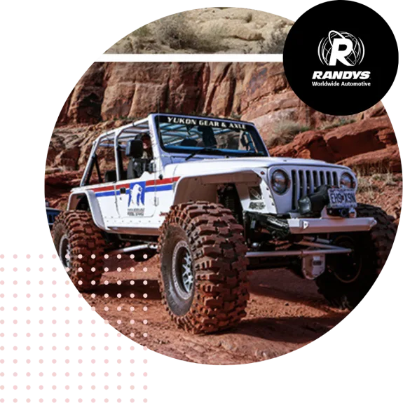 White jeep with large tires off-roading on rocky terrain with Randys logo.